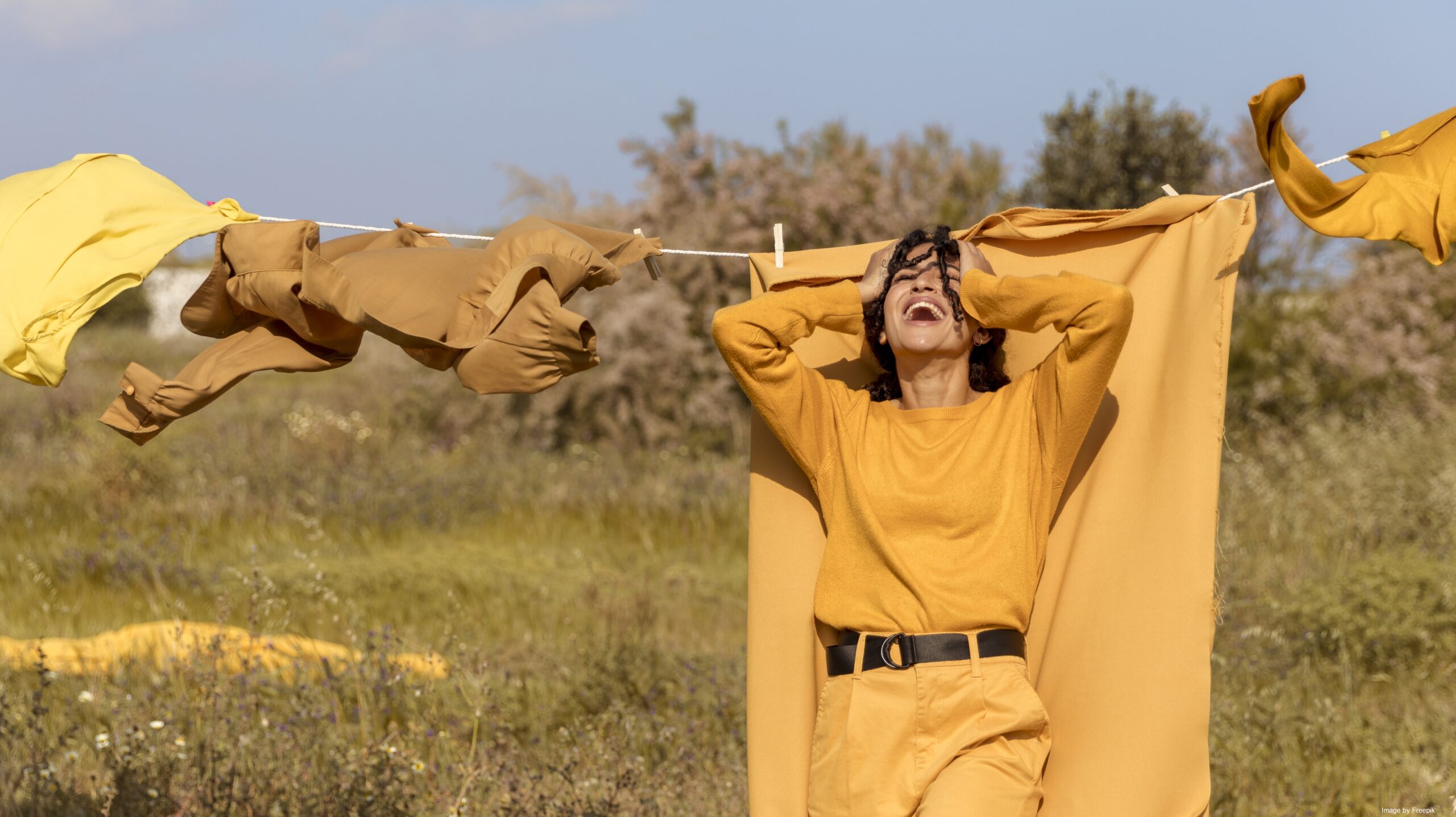 An image of a woman standing in front of a clothes line with a vibrant marigold color in an open field.