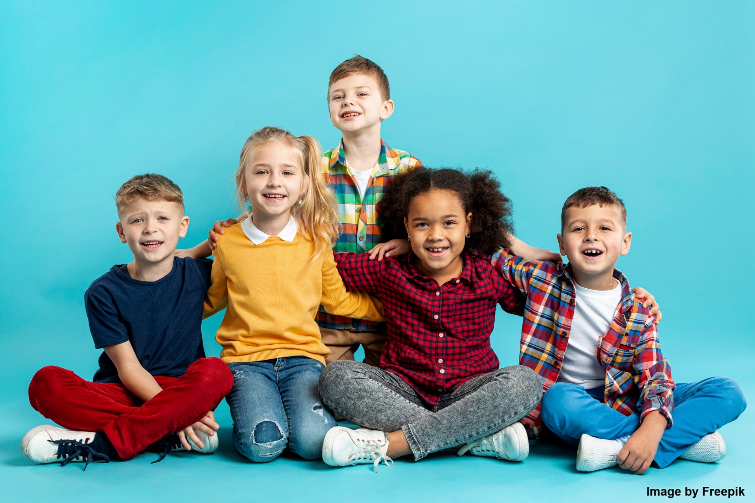 A group of five children sitting together, smiling and wearing colorful, eco-friendly kids' fashion, against a bright blue background.